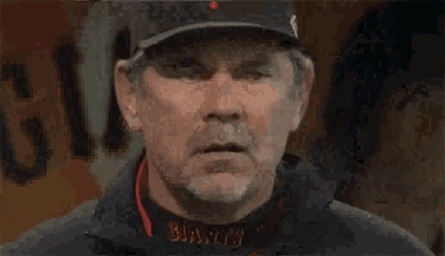 a man with a beard wearing a baseball cap and a jacket with the word busycity on it .