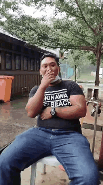 a man wearing a okinawa beach shirt sits on a chair