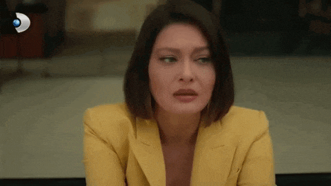 a woman in a yellow suit is sitting down and looking at the camera .