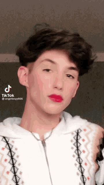 a young man wearing red lipstick and a white sweater has a tik tok sticker on his face