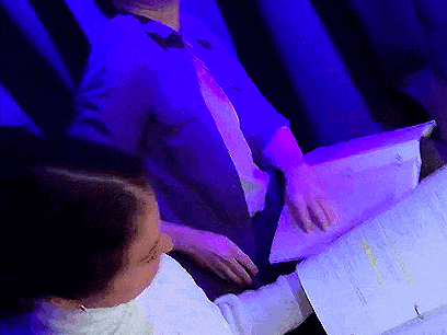 a man in a suit and tie sits next to a woman holding papers