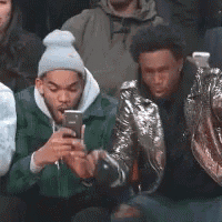 a group of young men are sitting in a crowd looking at their cell phones .