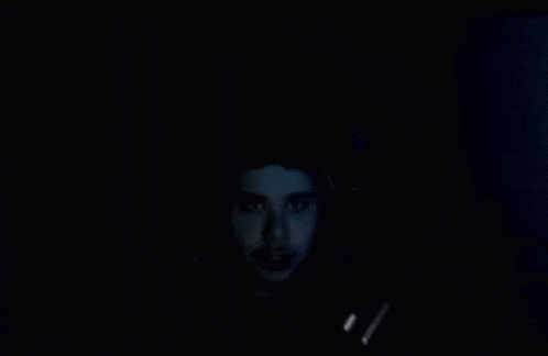 a man is looking at a computer screen in the dark with headphones on .