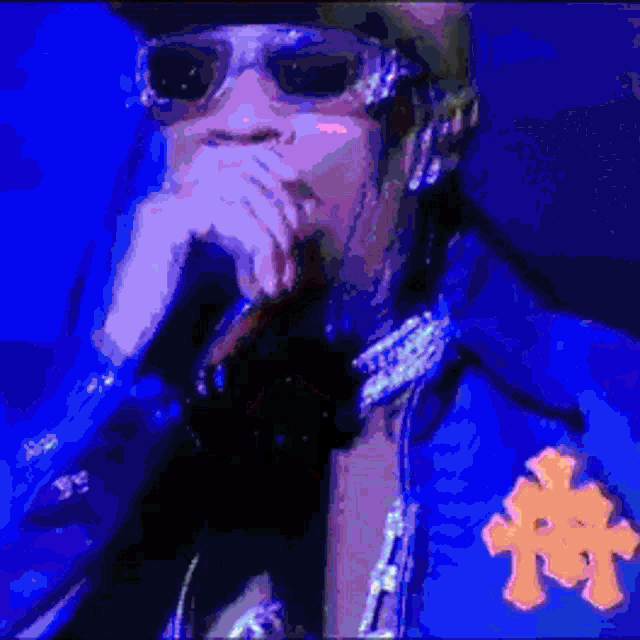 a pixelated image of a man wearing sunglasses and a blue jacket with the letter t on it