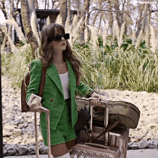 a woman in a green suit is pulling a suitcase and carrying a guitar case
