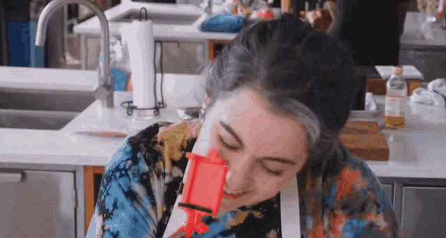 a woman wearing a tie dye shirt is holding a red object in front of her face
