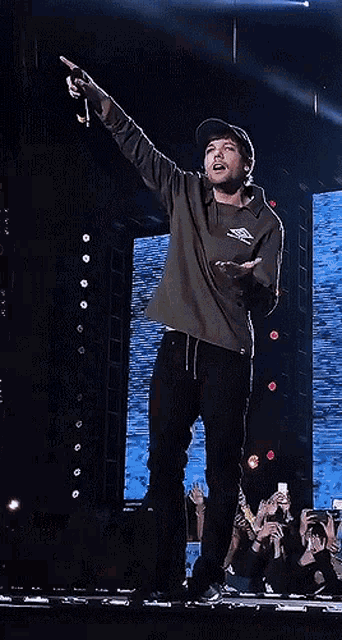 a man wearing a hat and a hoodie is holding a microphone and pointing up