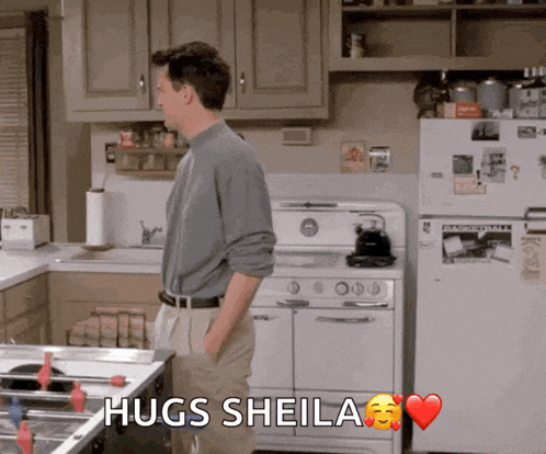 a man in a kitchen says hugs sheila with a heart