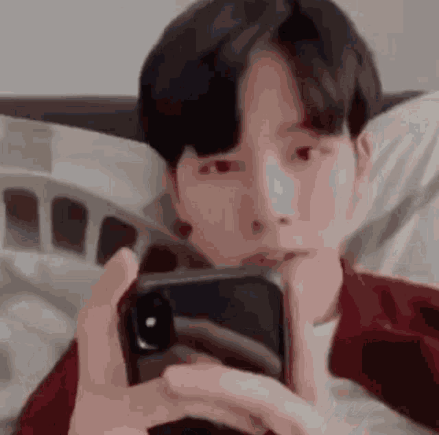 a young man is laying in bed holding a cell phone .
