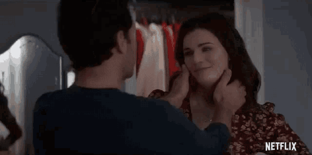 a man is putting a necklace on a woman 's neck in a closet .