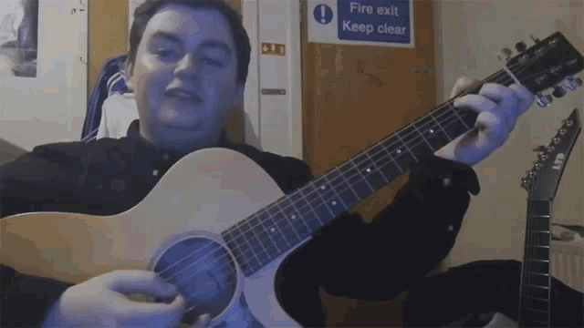 a man plays a guitar in front of a fire exit sign
