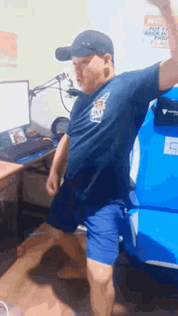a man wearing a hat and shorts is standing in front of a computer .