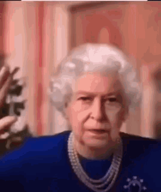 the queen is wearing a blue shirt and a pearl necklace while talking .