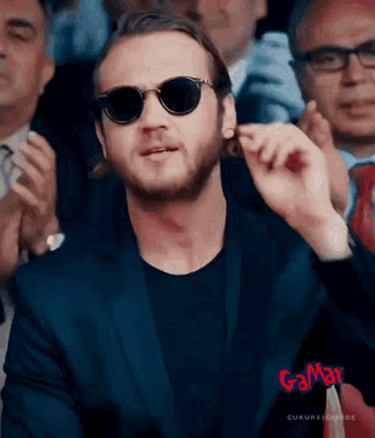 a man in a suit and sunglasses is sitting in a crowd