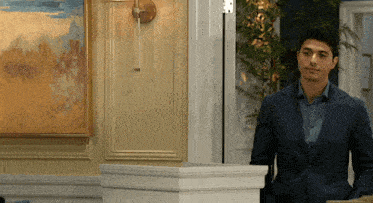a man in a suit stands in front of a wall with a painting on it