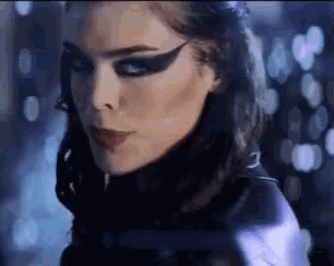 a close up of a woman 's face with dark makeup and a purple jacket on .