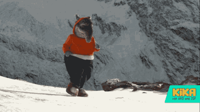 a stuffed animal with a red sweater and black pants is standing on a snowy hillside with a kiki logo in the background