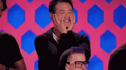 a man is covering his face with his hands and smiling while sitting in front of a pink background .