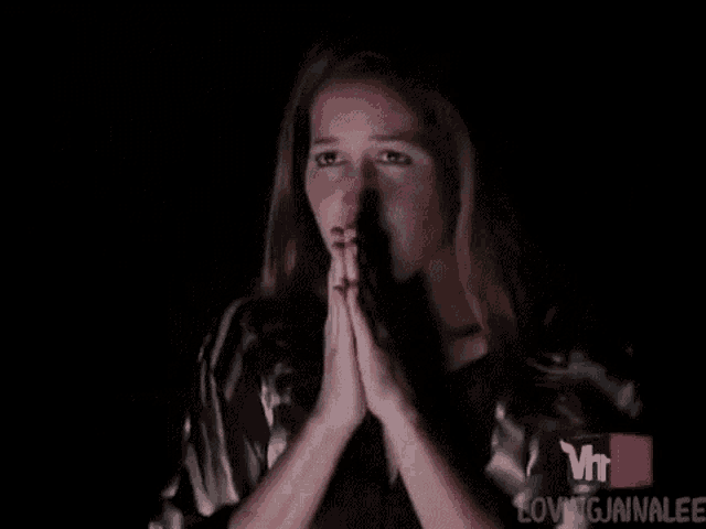 a woman is praying with her hands folded in front of her face in a dark room .