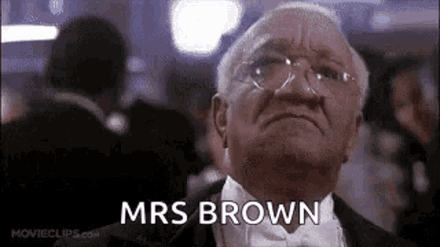 a man in a tuxedo and bow tie is saying `` mrs brown '' in a crowded room .