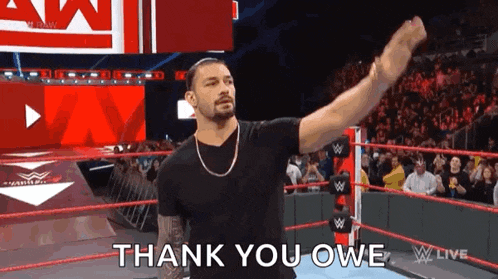 roman reigns is standing in the middle of a wrestling ring with his fist in the air and says thank you owe .