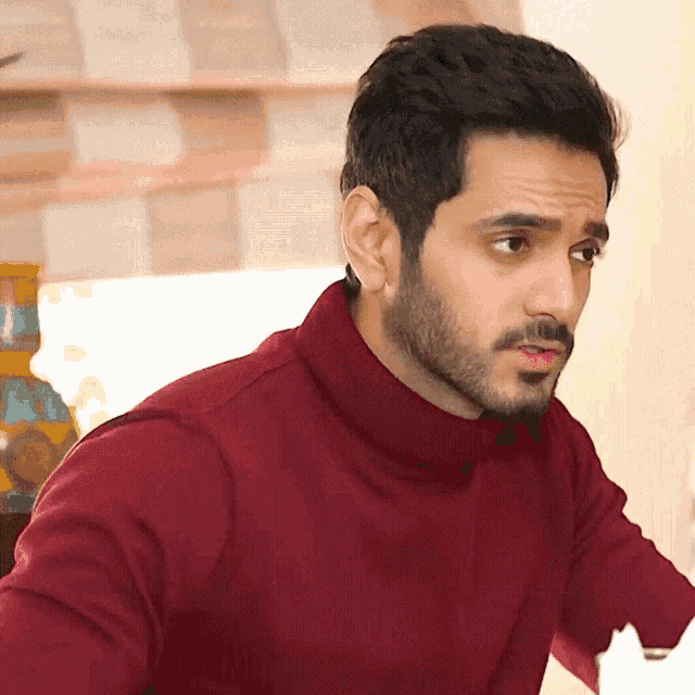 a man with a beard is wearing a maroon turtleneck