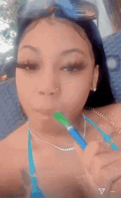 a girl in a bikini is brushing her teeth with a green toothbrush .
