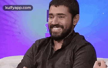 a man with a beard is smiling while sitting on a white couch .