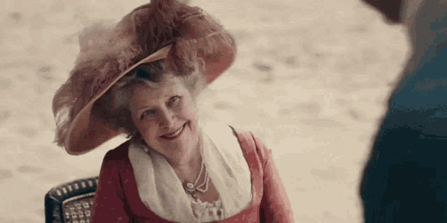 a woman wearing a large hat and a red dress is smiling
