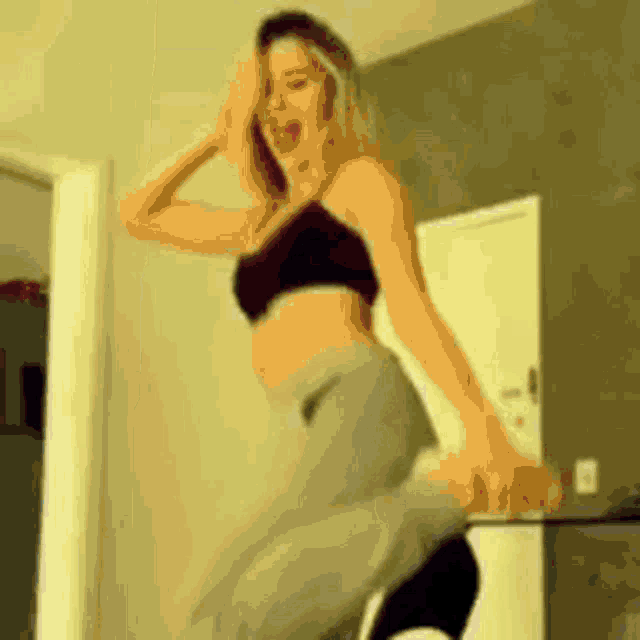 a woman in a black bra and gray pants is jumping in the air .