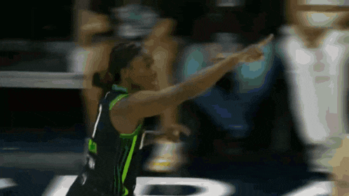 a basketball player in a black and green uniform is pointing at the camera