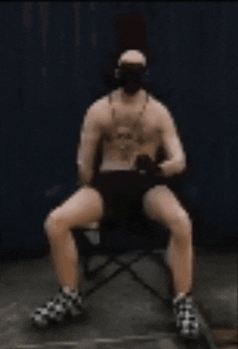 a shirtless man is sitting in a chair with his legs crossed and a mask on his face .