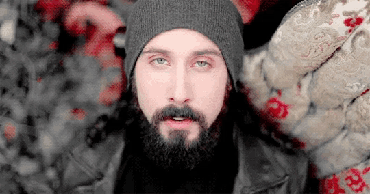 a man with a beard wearing a beanie and a black jacket .
