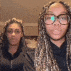 two women wearing glasses and braids are standing next to each other and looking at the camera .