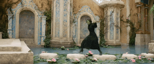 a woman in a black dress is standing on a rock in the water