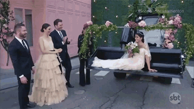 a bride and groom are standing next to a carriage with a bride laying in the back .