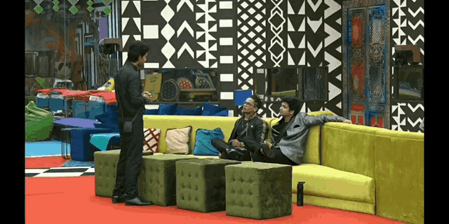 three men are sitting on a yellow couch in a room