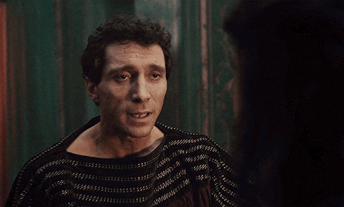 a man in a black and white sweater looks at a woman in a dark room