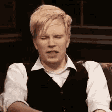 a man in a white shirt and black vest is sitting on a couch .