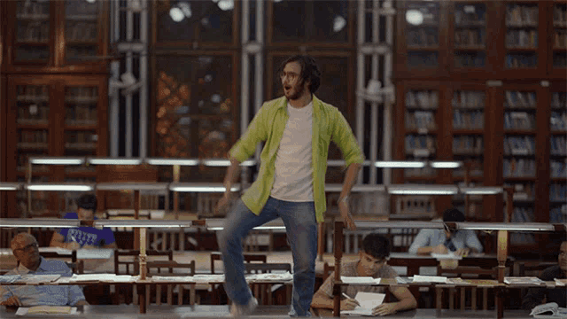 a man in a green shirt is dancing in a library with students