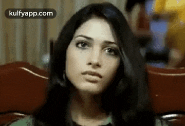 a woman with long black hair is sitting in a chair and making a funny face .