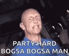 a bald man in a blue shirt is making a funny face while sitting in a chair .