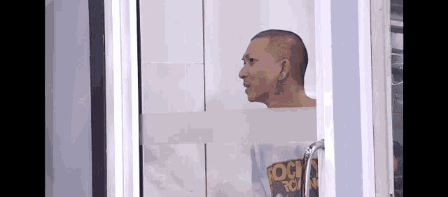 a man with a shaved head is standing in front of a window .