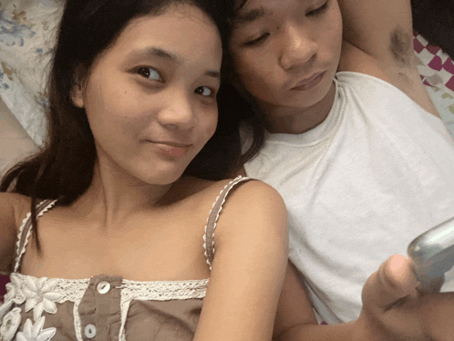 a man and a woman are laying on a bed and the woman is holding a cell phone