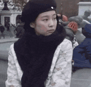 a woman wearing a beret and scarf is standing in a crowded street .