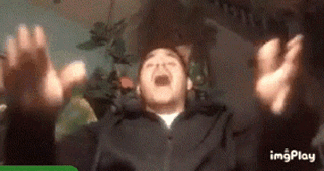 a man in a black jacket is screaming with his hands in the air