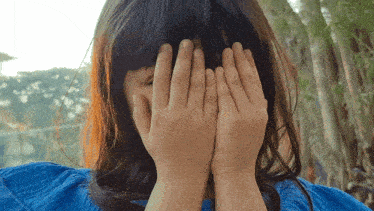 a woman covering her face with her hands in a blue dress