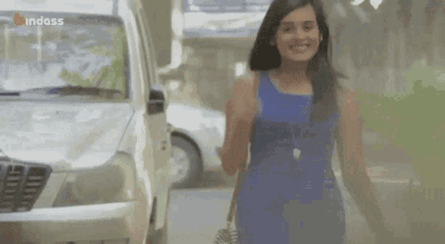 a woman in a blue dress is walking down a street with a white car in the background