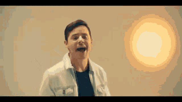 a man in a white jacket and black shirt is standing in front of a light .