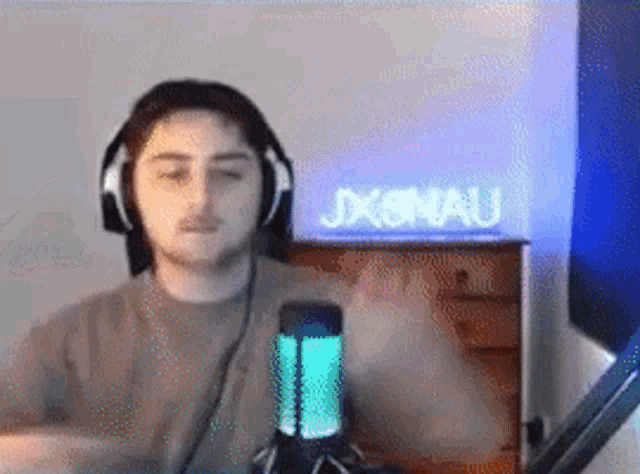 a man wearing headphones is sitting in front of a microphone and a neon sign that says jxonau .